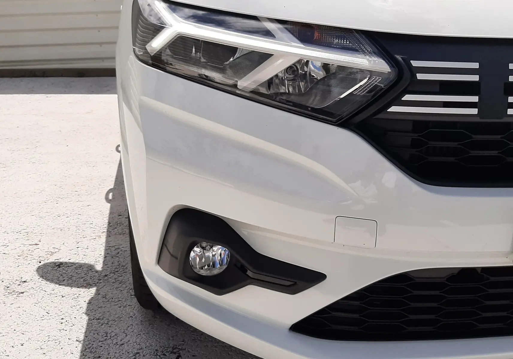 Gros plan sur l'avant droit blanc glacier d'une Dacia Sandero 2024, mettant en valeur le phare LED et la calandre noire.