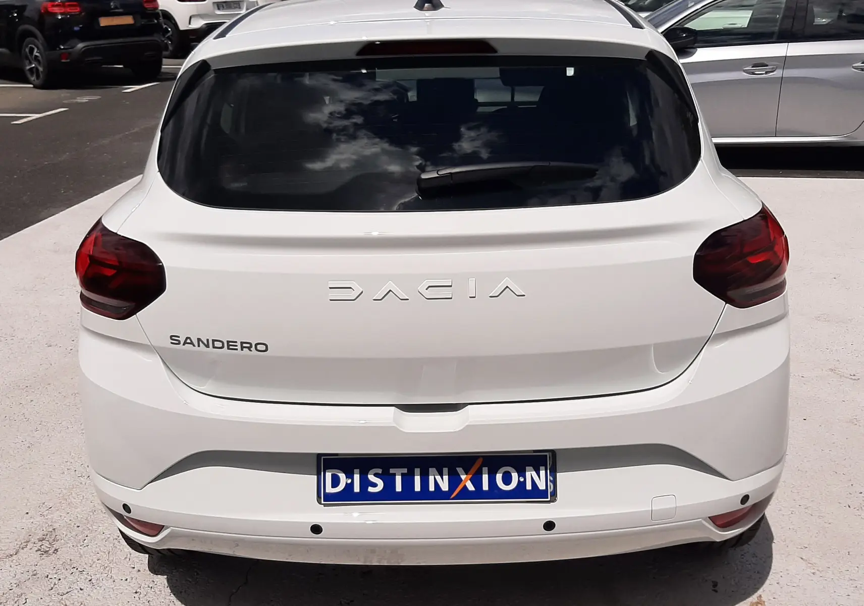 Vue arrière d'une Dacia Sandero blanc glacier 2024 avec feux arrière rouges et plaque d'immatriculation Distinxion.