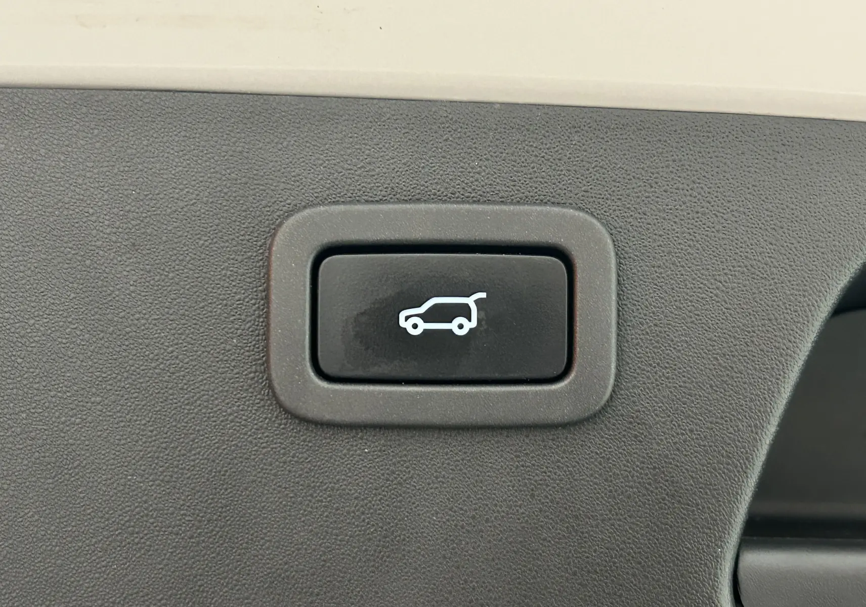 Bouton noir de hayon électrique avec pictogramme blanc de voiture et coffre ouvert sur fond beige intérieur Jaguar E-PACE 2018.