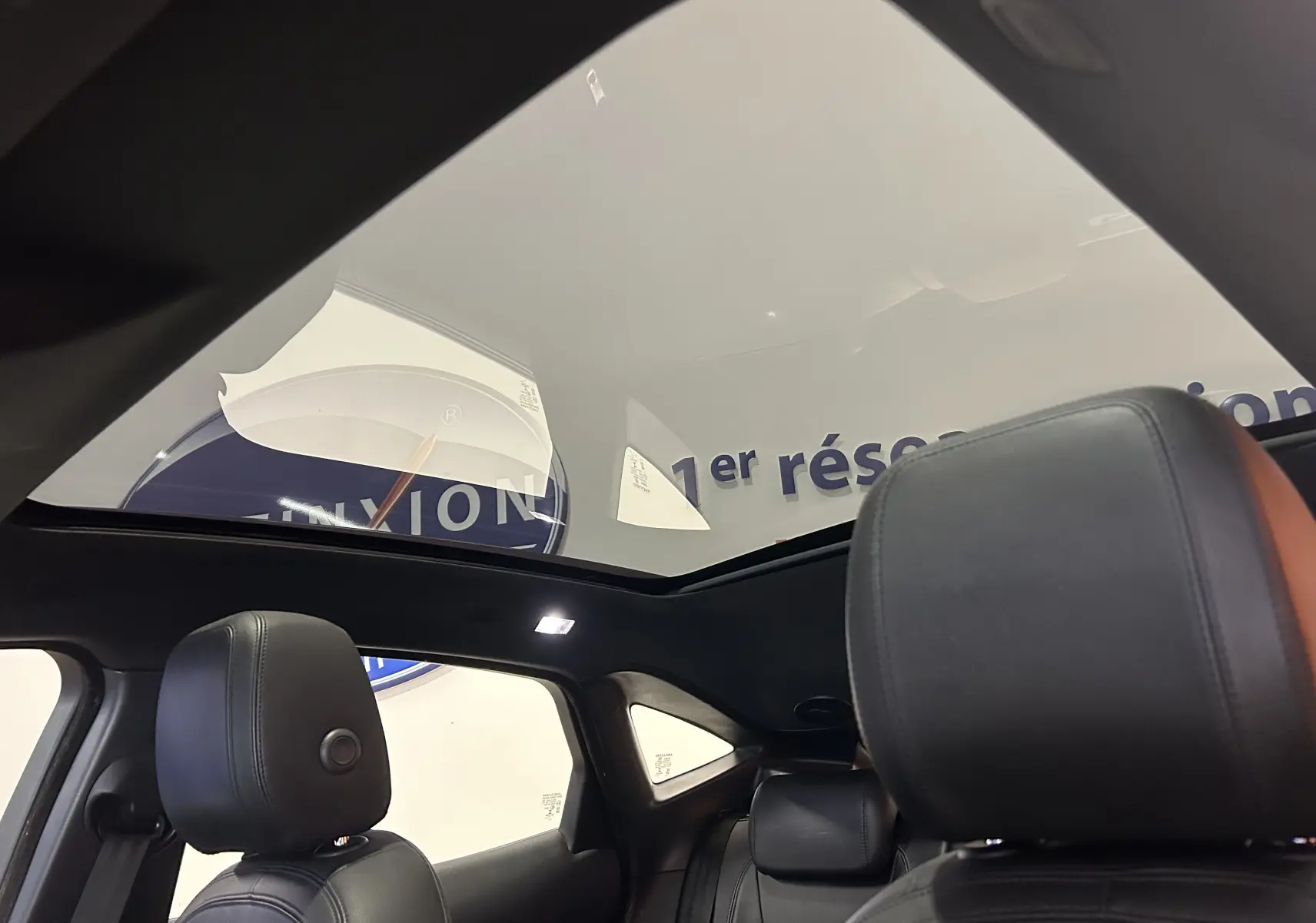 Vue intérieure du toit panoramique du Jaguar E-PACE beige 2018, avec sièges en cuir noir et éclairage LED.