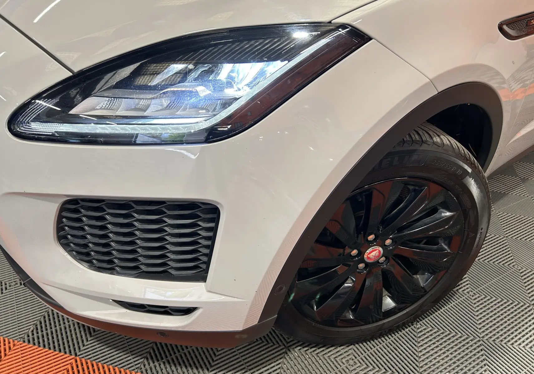Gros plan sur l'avant droit beige du Jaguar E-PACE 2018, mettant en valeur le phare LED et la jante noire brillante.