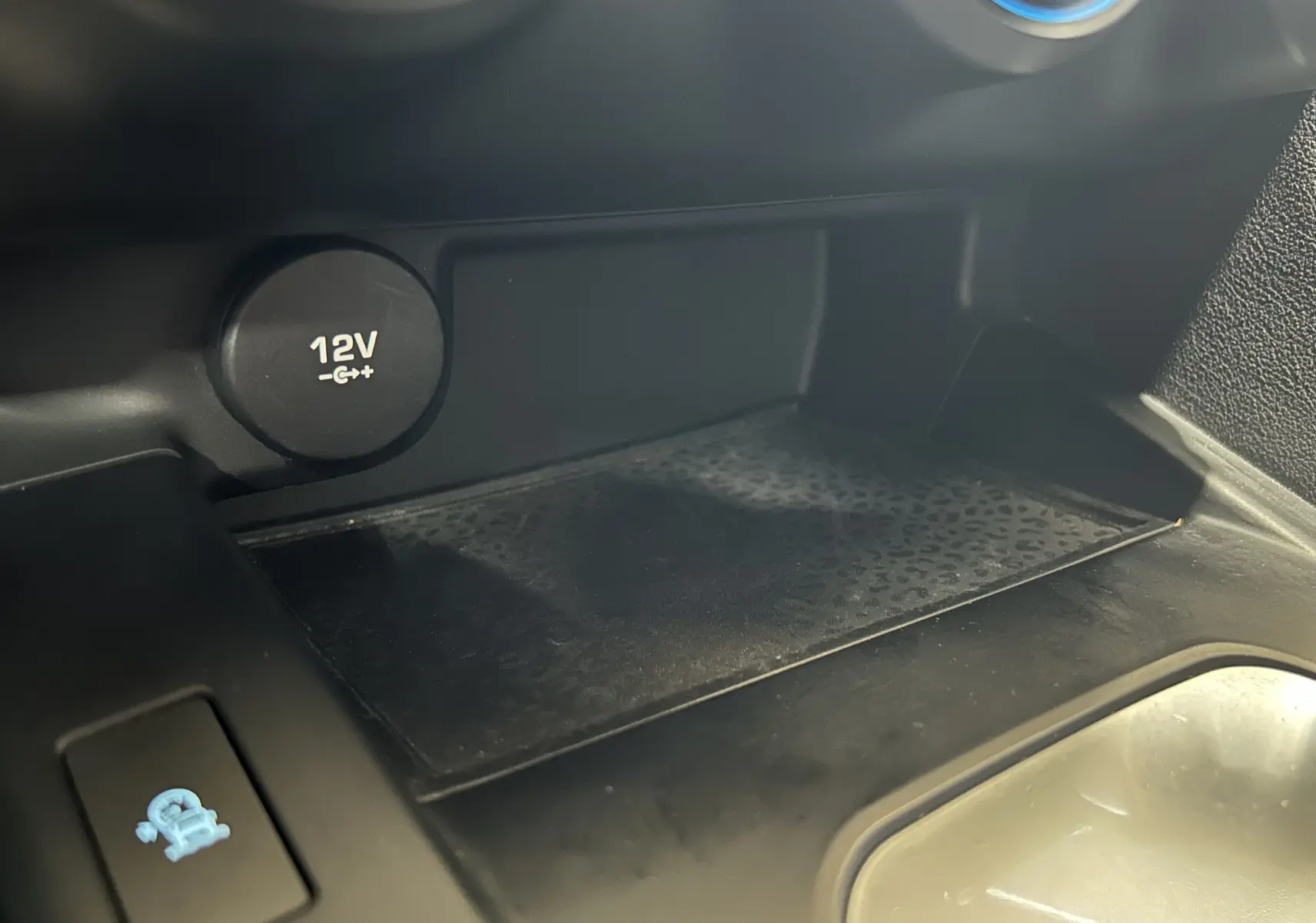 Détail de la prise 12V et du compartiment de rangement intérieur du Jaguar E-PACE beige, vue rapprochée côté console centrale.