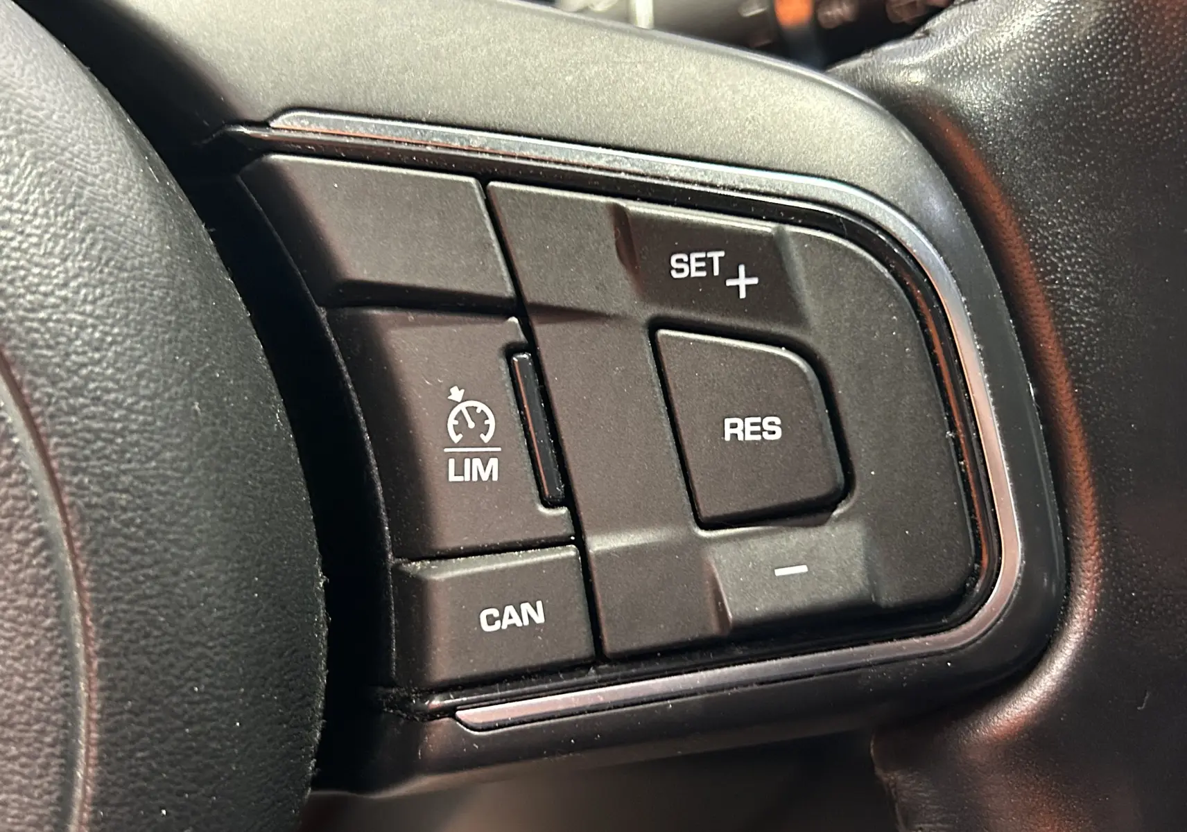 Gros plan sur les commandes de régulateur de vitesse au volant d’un Jaguar E-PACE beige, intérieur noir.