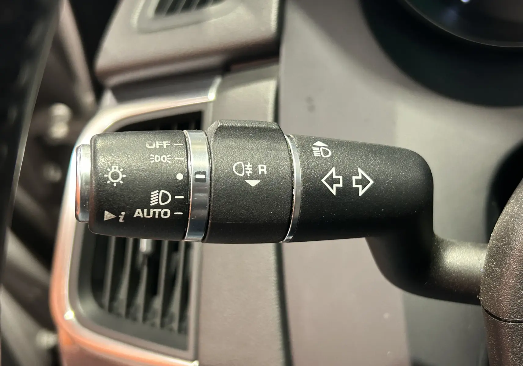 Gros plan sur la commande de clignotants et phares du Jaguar E-PACE beige, avec les symboles lumineux visibles.