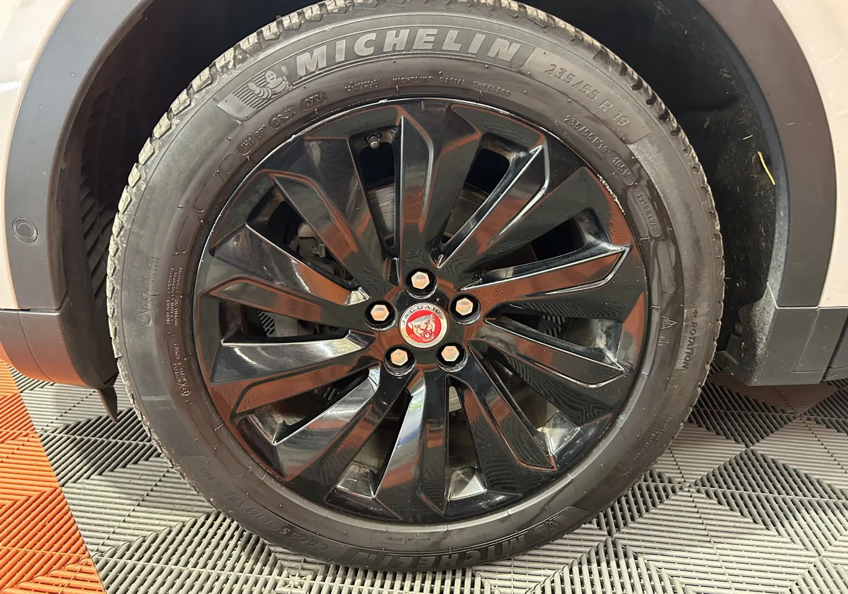 Gros plan sur la roue avant droite noire brillante du Jaguar E-PACE beige avec logo Jaguar rouge au centre.
