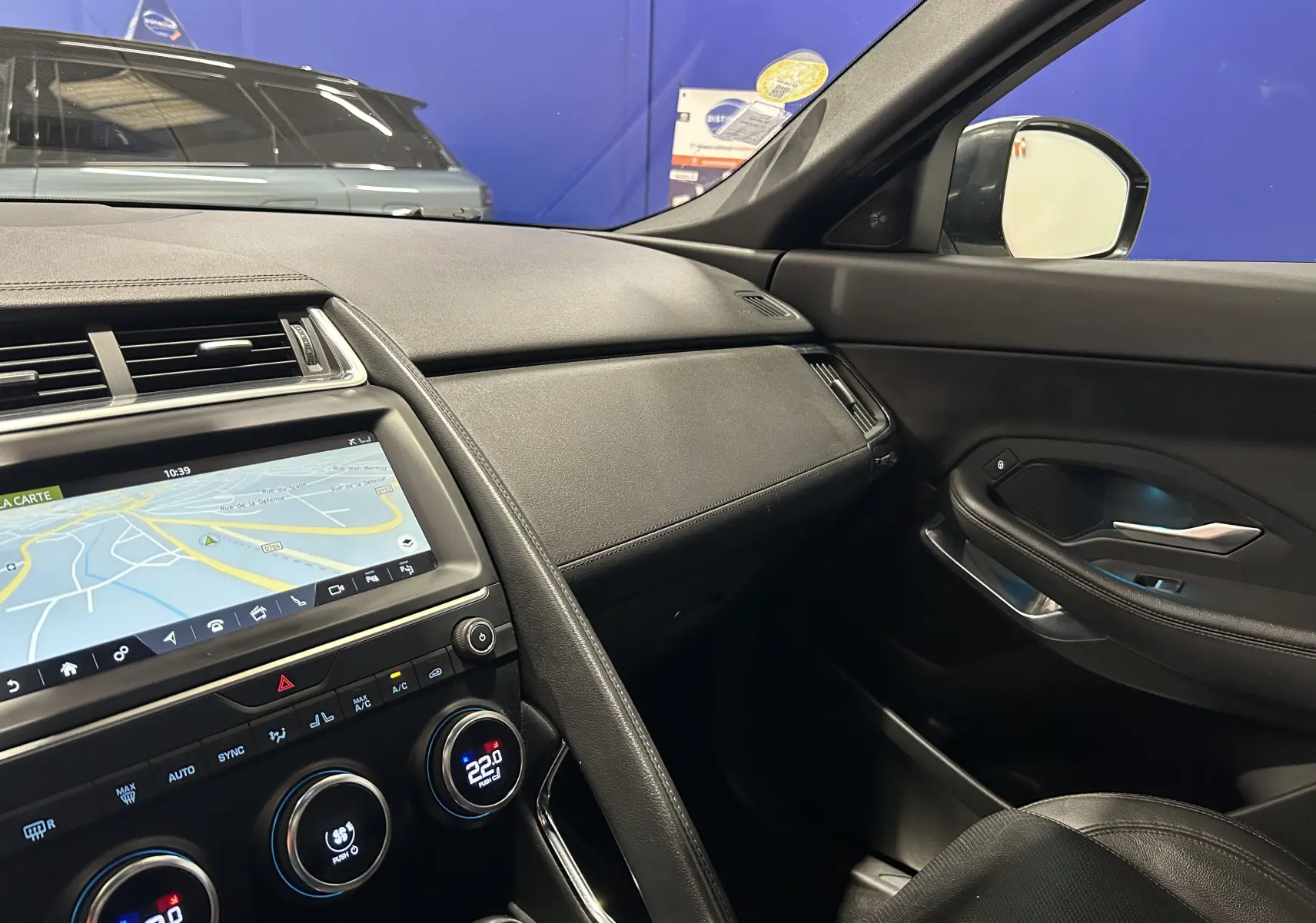 Vue intérieure côté passager du tableau de bord et de la porte d’une Jaguar E-Pace beige, avec écran tactile et climatisation digitale.
