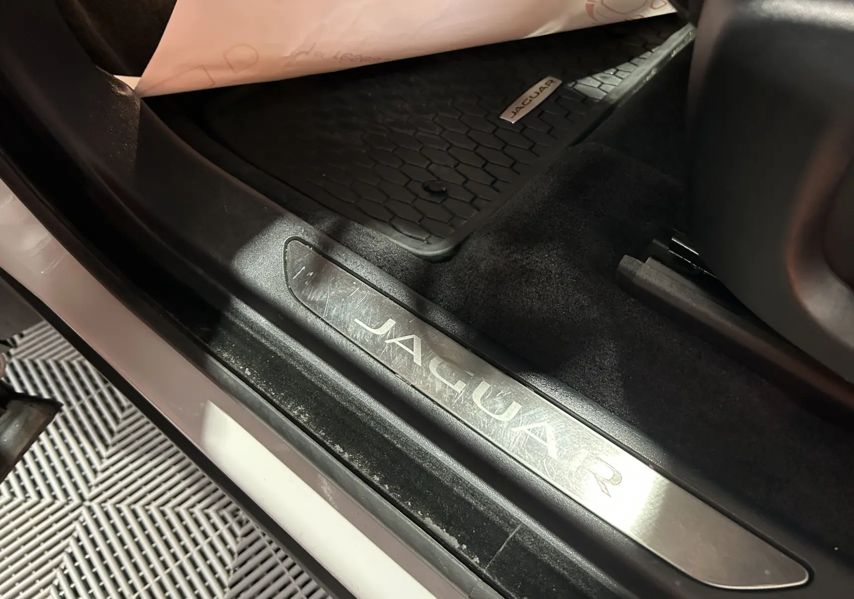 Gros plan sur la plaque de seuil de porte Jaguar côté conducteur avec tapis de sol noir et intérieur sombre.