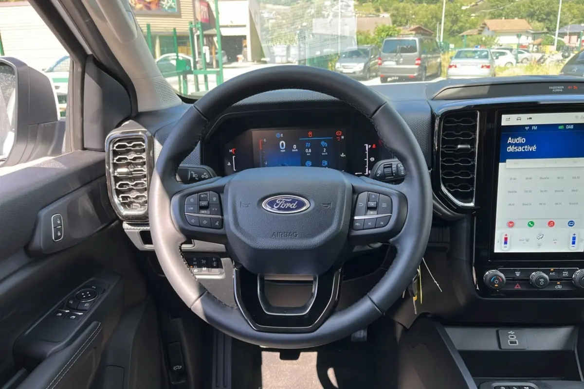 Intérieur du Ford Ranger 2025 gris carbone, vue centrée sur le volant multifonction et l'écran tactile du tableau de bord.