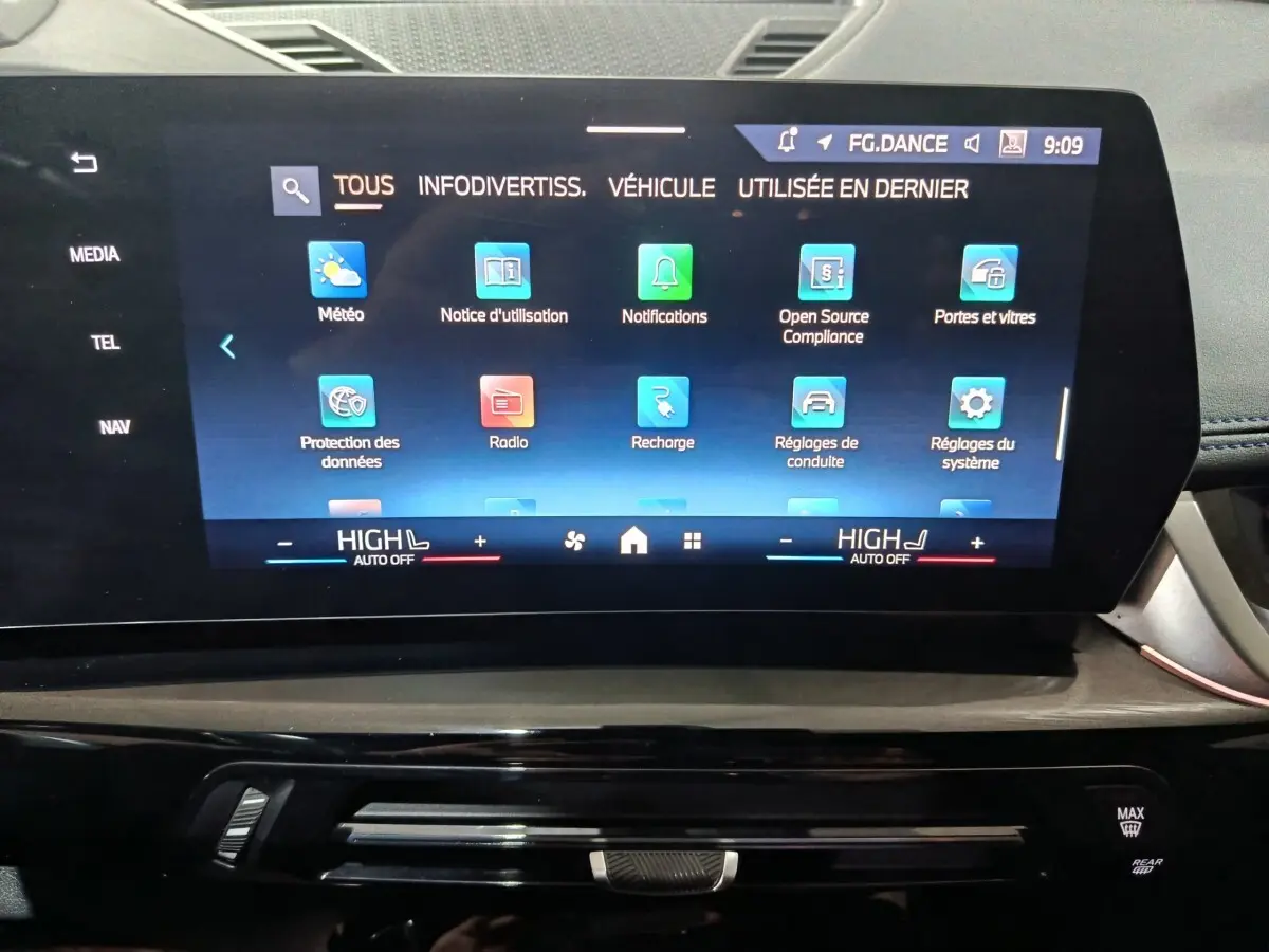 Écran tactile central du tableau de bord du BMW X1 blanc, affichant le menu principal multimédia et réglages.