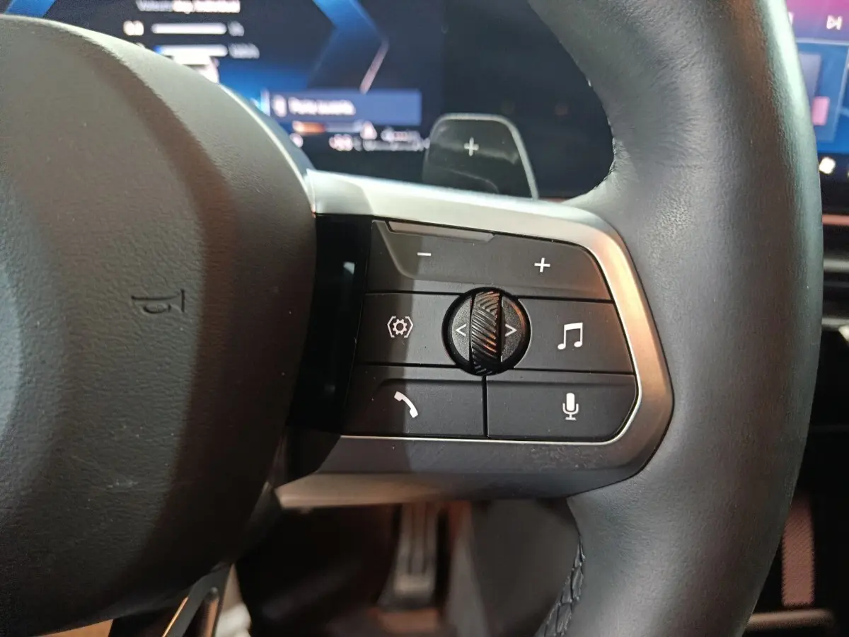 Gros plan sur les commandes multifonctions du volant cuir noir du BMW X1 xDrive25e blanc, version 2024.