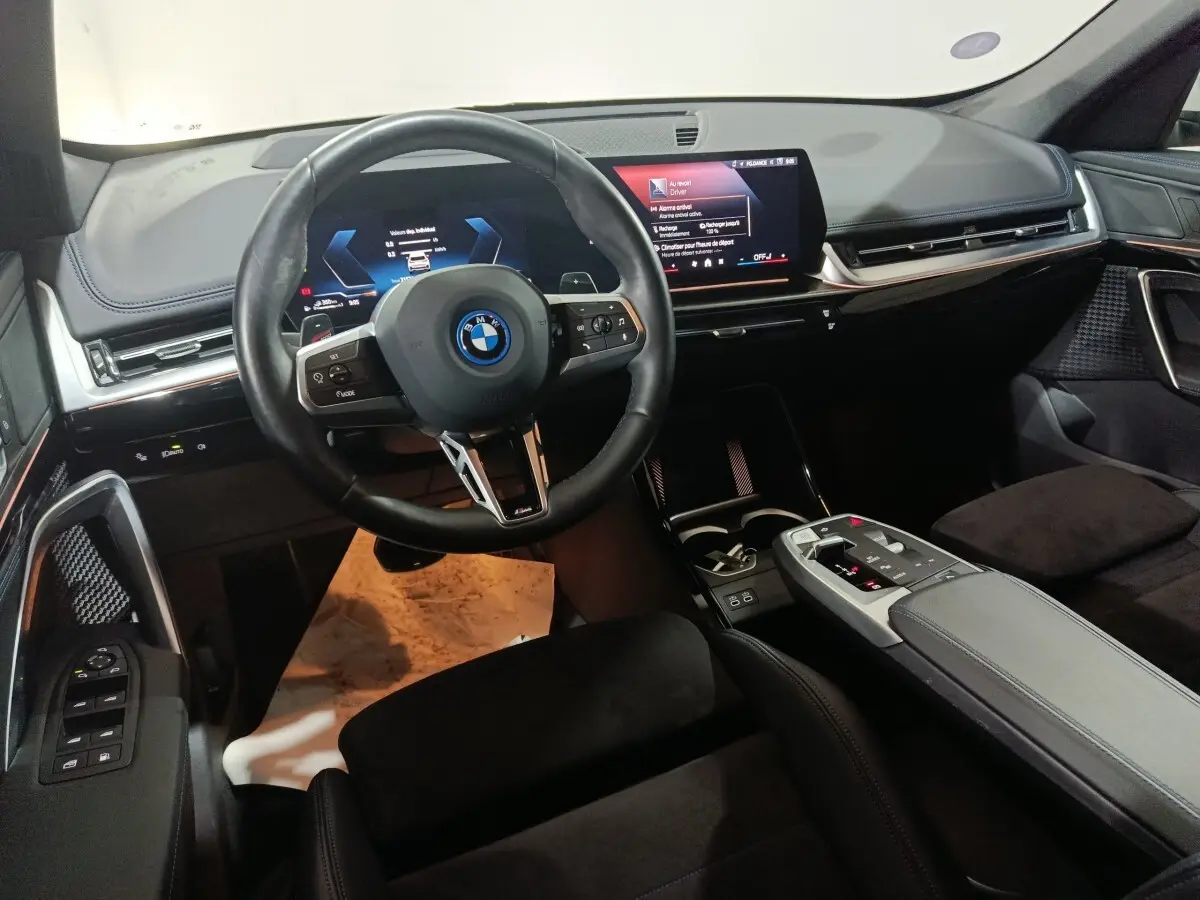 Vue intérieure du tableau de bord et volant noir du BMW X1 xDrive25e M Sport 2024 avec écran tactile central.