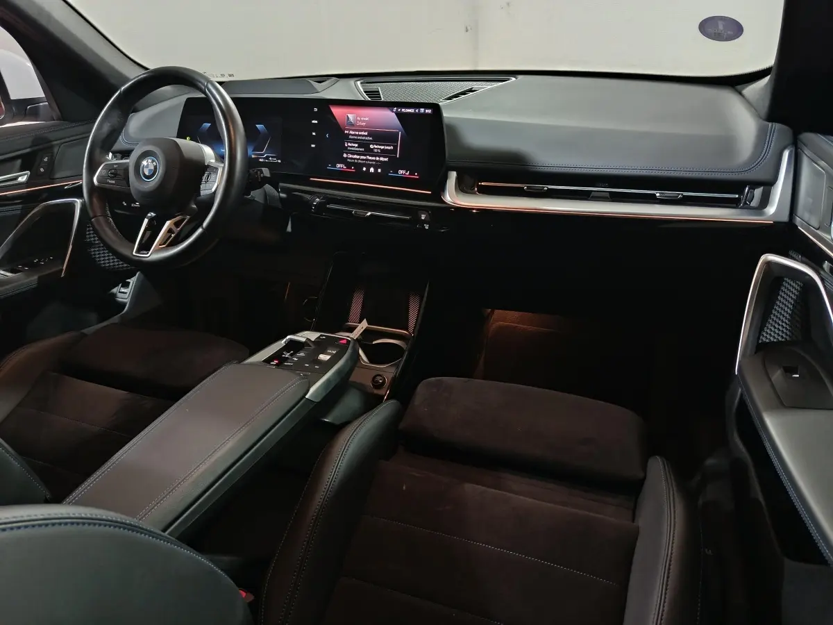 Intérieur BMW X1 xDrive25e 2024 vu de l'avant, tableau de bord noir avec écran tactile large et volant cuir multifonctions.