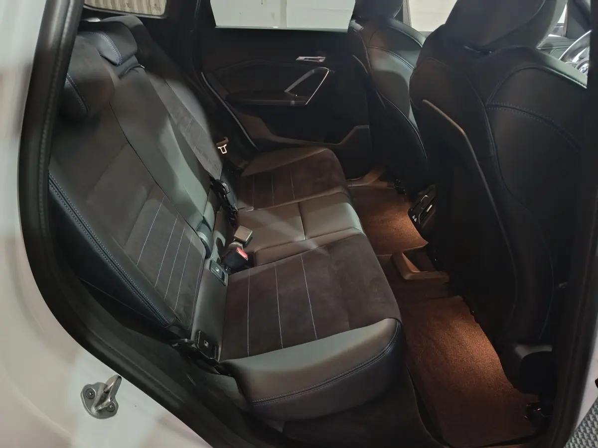 Vue intérieure côté gauche des sièges arrière en cuir noir et alcantara du BMW X1 xDrive25e blanc 2024.
