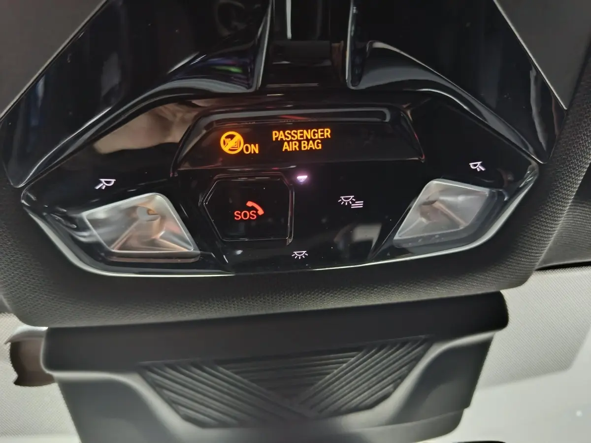 Gros plan sur la console de plafonnier noire du BMW X1 blanc, avec indicateur airbag passager et bouton SOS éclairés.