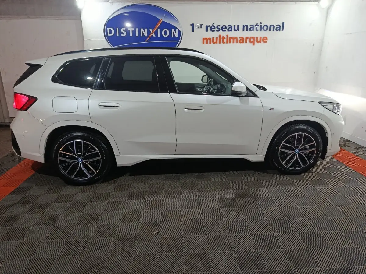 Vue de profil côté gauche d'un BMW X1 blanc xDrive25e M Sport 2024 avec jantes noires et logo M Sport visible.