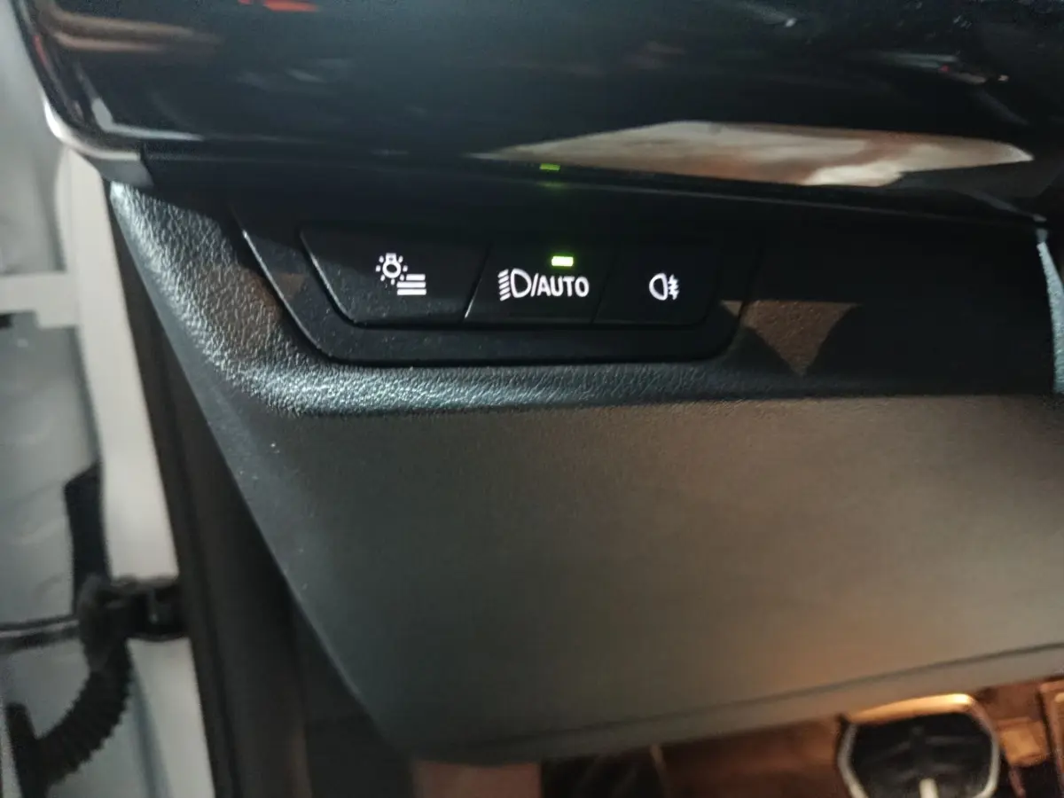 Détail des commandes d’éclairage avec bouton auto allumé sur BMW X1 blanc, vue intérieure côté conducteur.