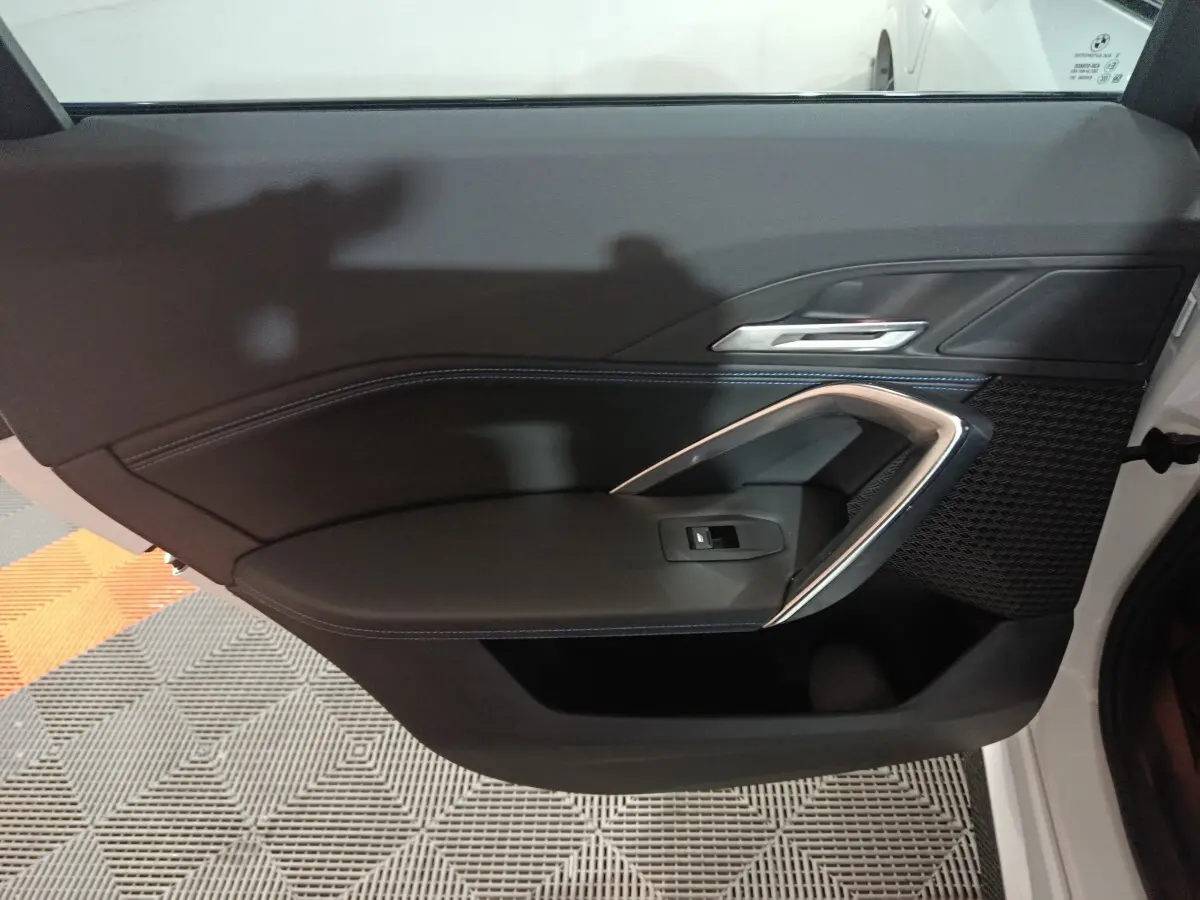 Intérieur de la porte avant gauche noire du BMW X1 xDrive25e blanc, avec poignée argentée et bouton de vitre électrique.