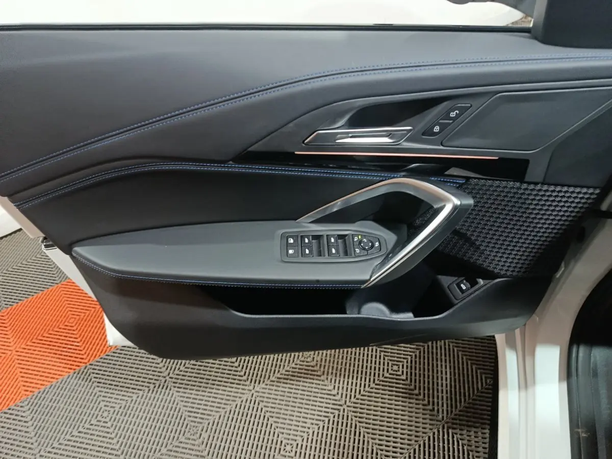 Vue intérieure côté gauche de la porte avant d’un BMW X1 blanc, avec commandes de vitres et surpiqûres bleues.