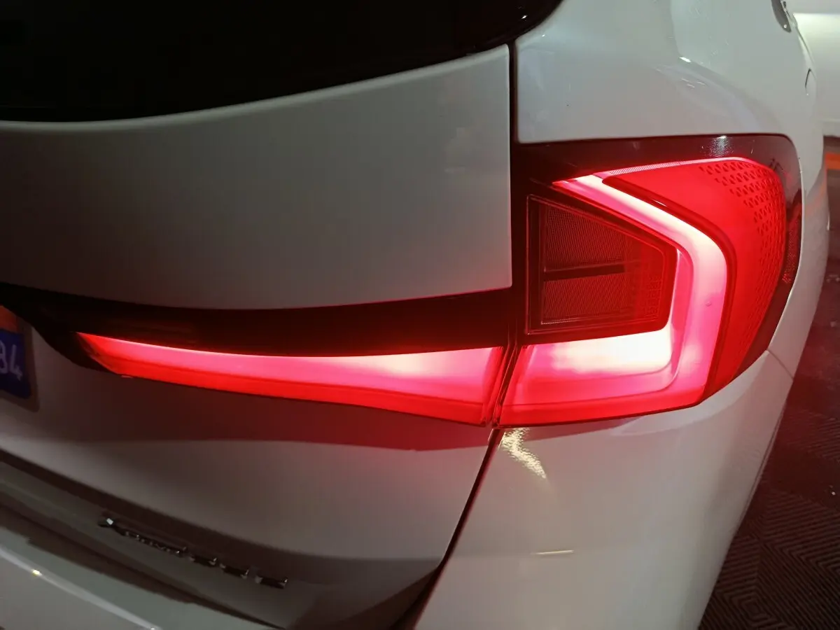 Gros plan sur le feu arrière droit rouge allumé d’un BMW X1 blanc, version xDrive25e M Sport 2024.