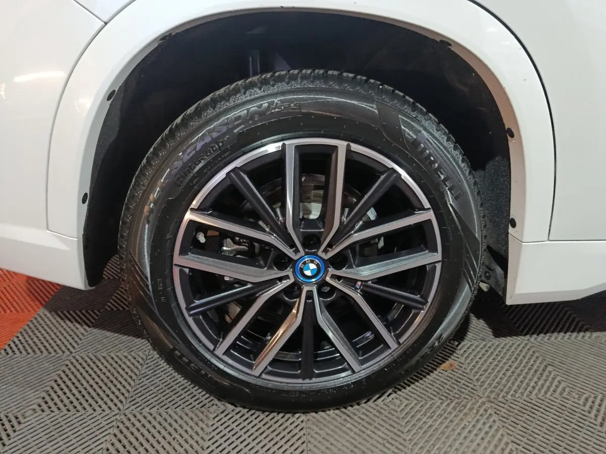 Gros plan sur la roue avant droite noire à jante alliage du BMW X1 blanc xDrive25e M Sport 2024.