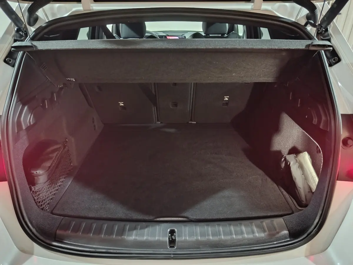 Coffre ouvert vu de l'arrière d'un BMW X1 blanc 2024, avec cache-bagages et intérieur noir épuré.