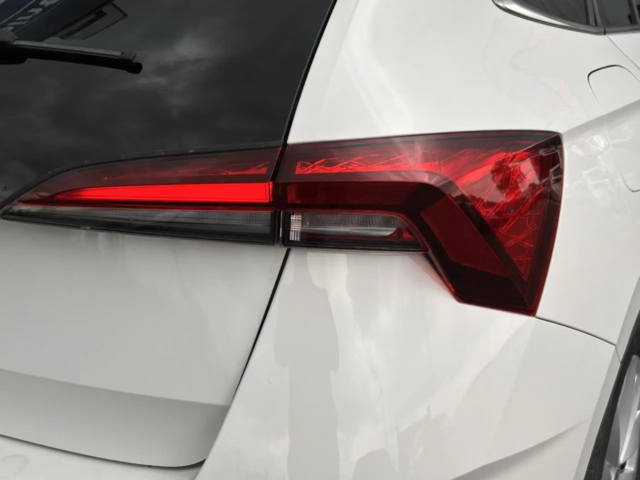 Gros plan sur le feu arrière droit rouge vif d’une Skoda Scala blanche Candy, avec lunette arrière surteintée visible.