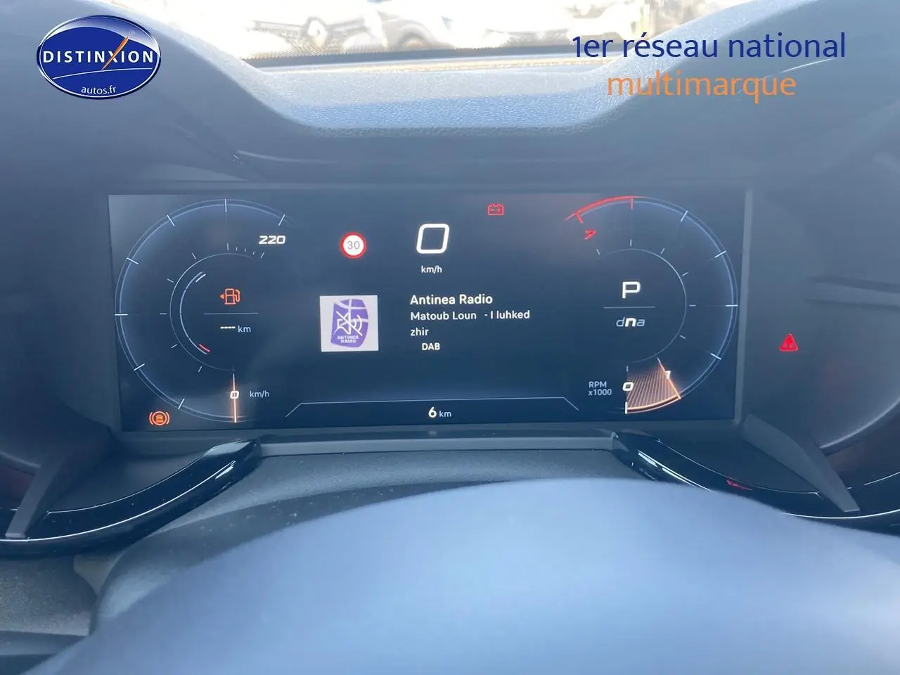 Vue rapprochée du tableau de bord numérique de l'Alfa Romeo Junior 1.2 hybride, affichant la radio et l'indicateur de vitesse.