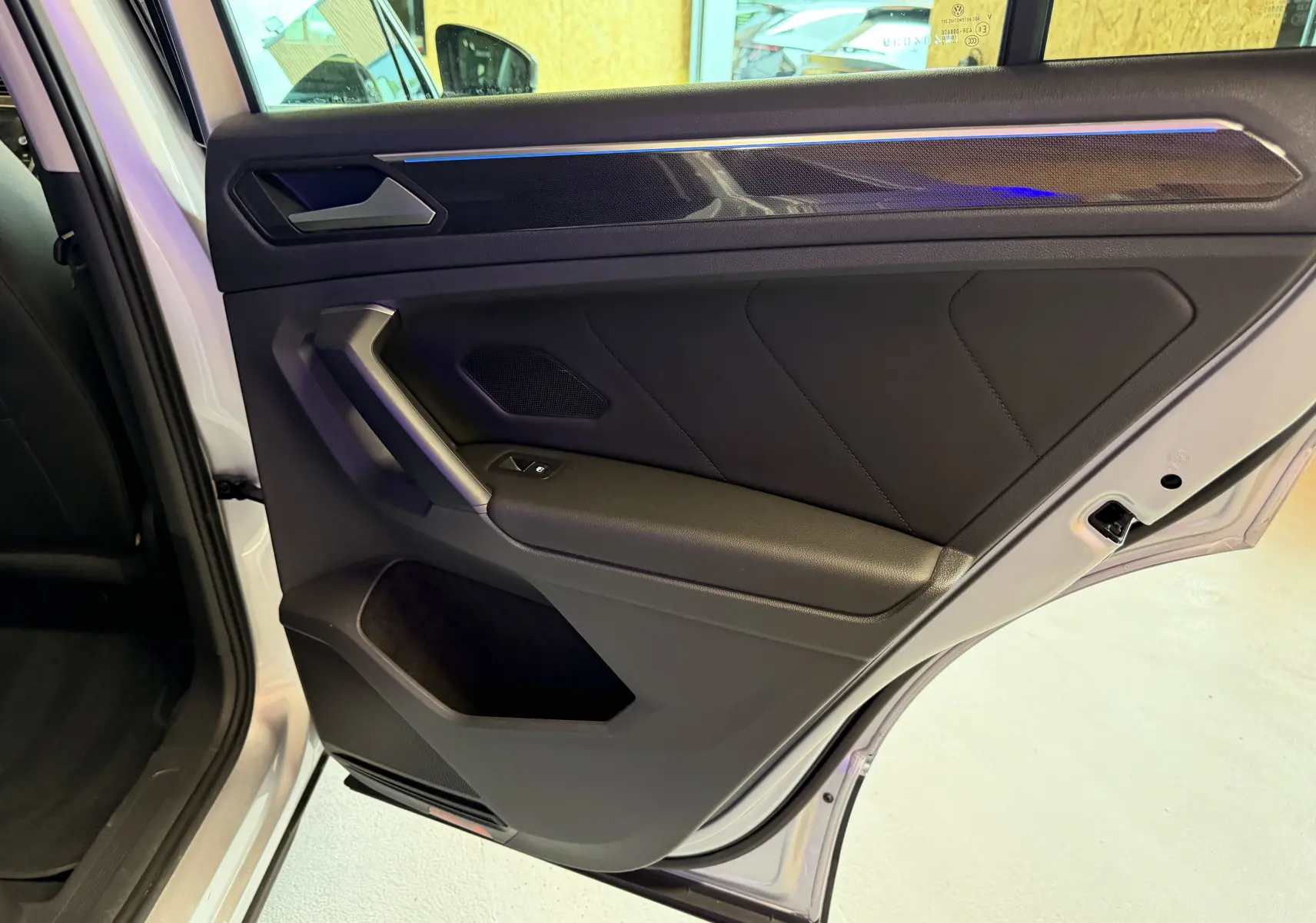 Vue intérieure de la porte arrière droite du Volkswagen Tiguan gris clair, avec garniture noire et poignée angulaire.