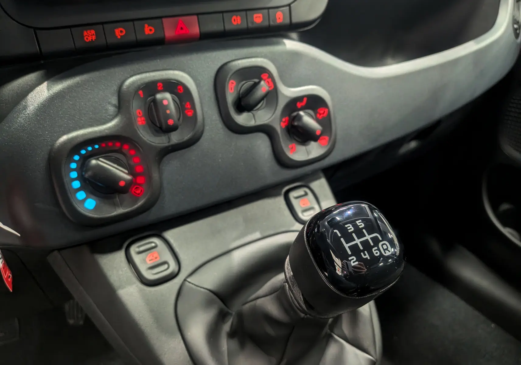 Gros plan sur le levier de vitesses manuel et les commandes de climatisation du tableau de bord noir de la Fiat Panda 2025.