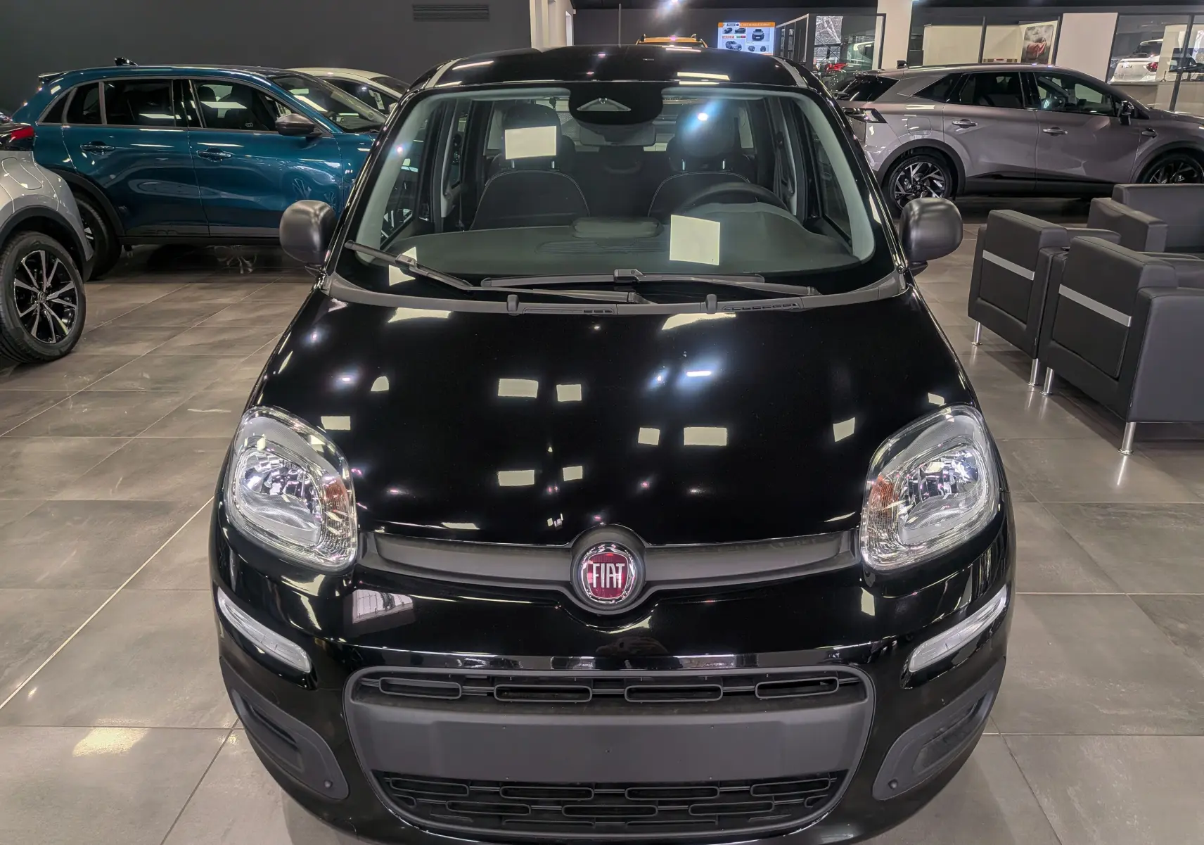 Vue frontale d'une Fiat Panda 1.0 70 CH Hybrid City noire, exposée en showroom avec ses phares et logo bien visibles.