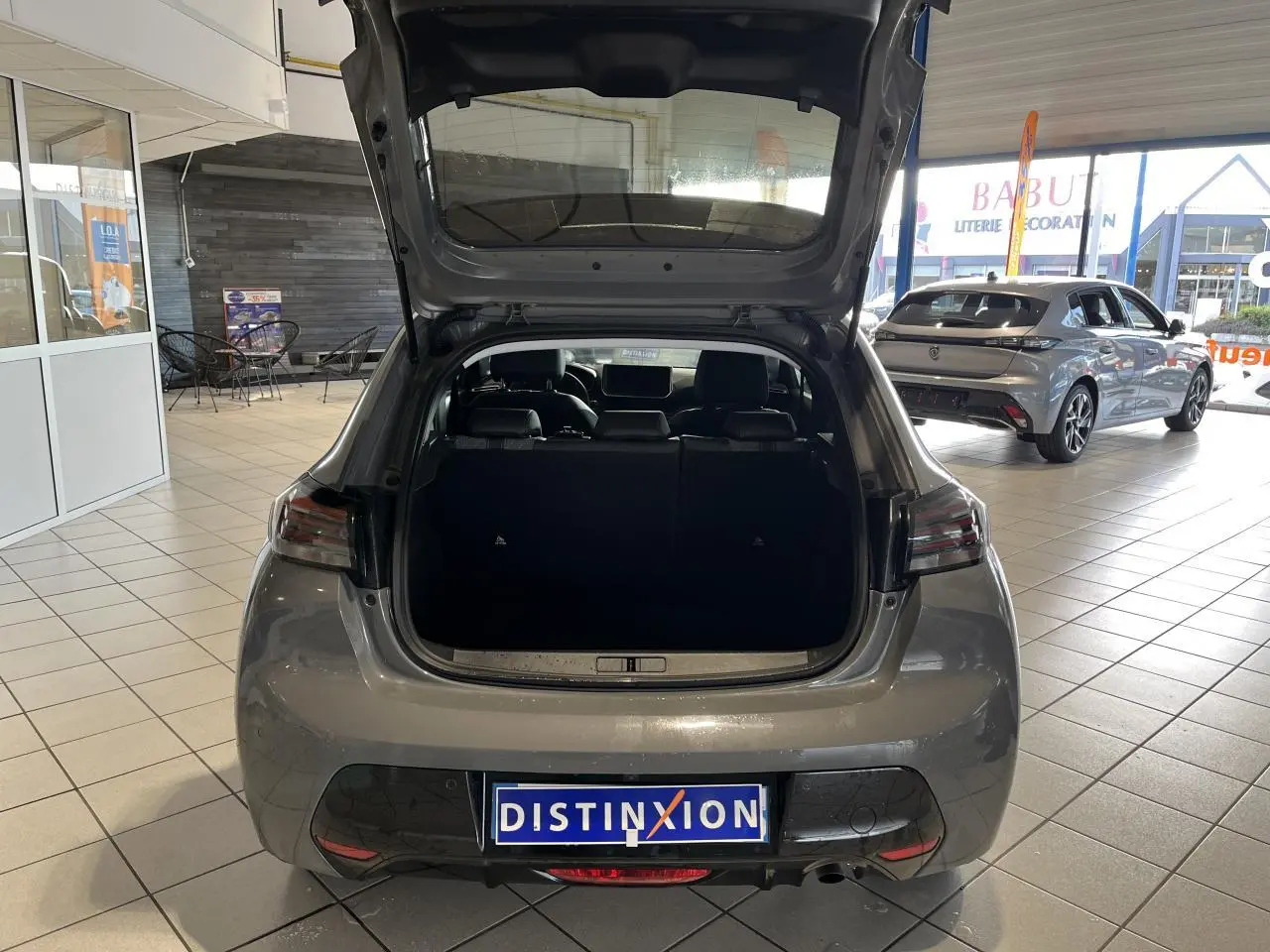 Vue arrière ouverte d'un Peugeot 208 gris clair Selenium en concession, avec feux arrière à LED et intérieur visible.