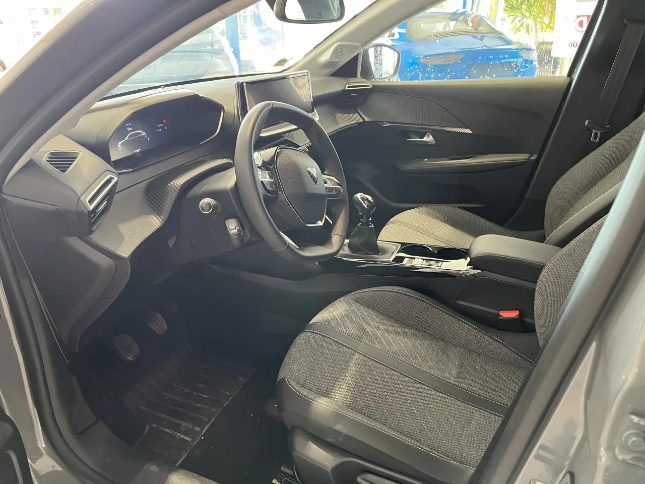 Intérieur avant droit du Peugeot 208 gris clair, volant compact cuir et sellerie tissu gris avec surpiqûres Quartz.
