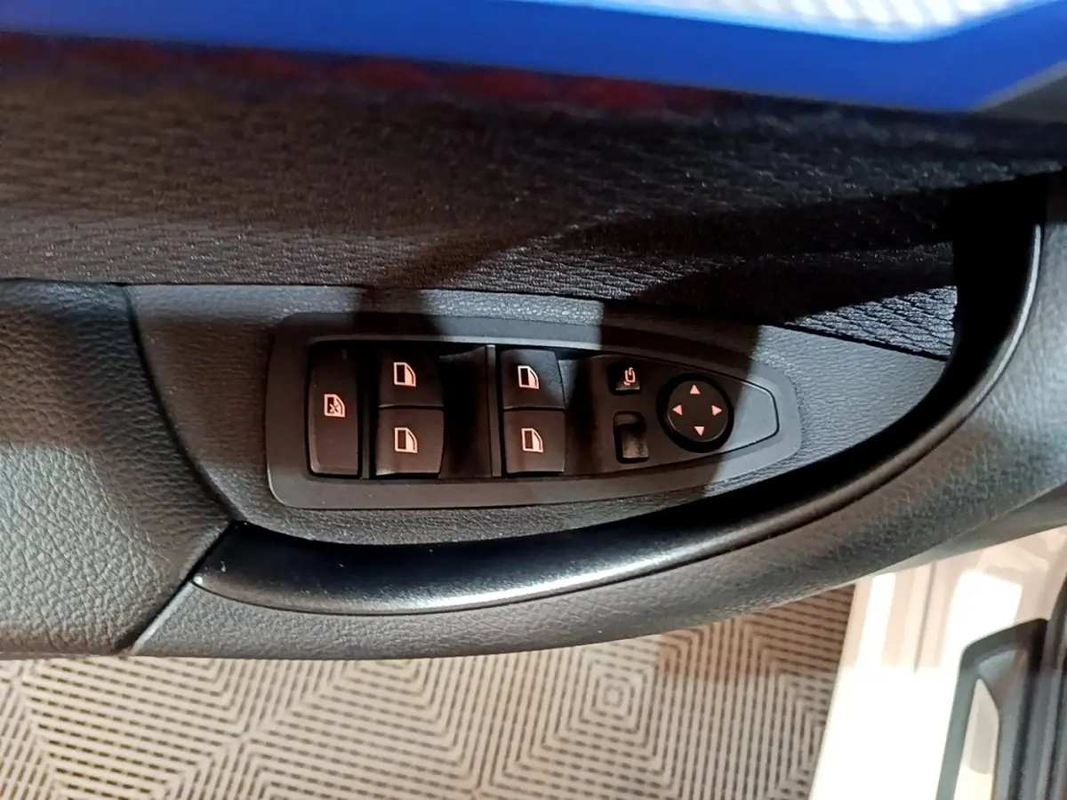 Gros plan sur les commandes des vitres électriques et rétroviseurs côté gauche d'une BMW X1 blanc 2022.