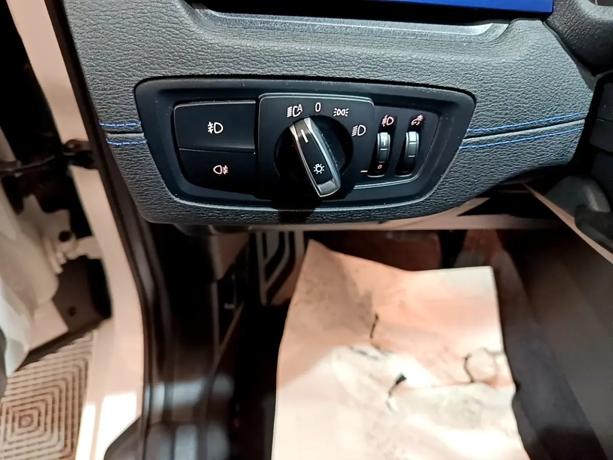 Détail du panneau de commande des phares sur la gauche du tableau de bord d’un BMW X1 blanc 2022.