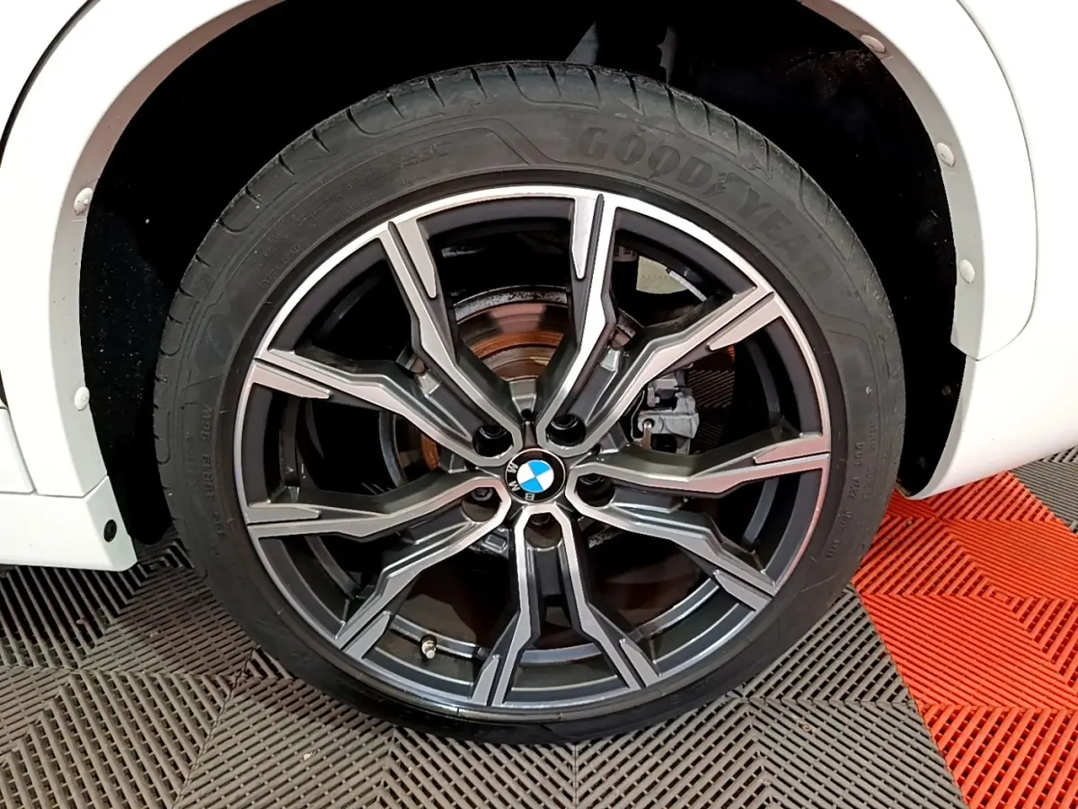 Gros plan sur la roue avant droite d’un BMW X1 blanc, jante alliage noire et argent avec logo BMW central.