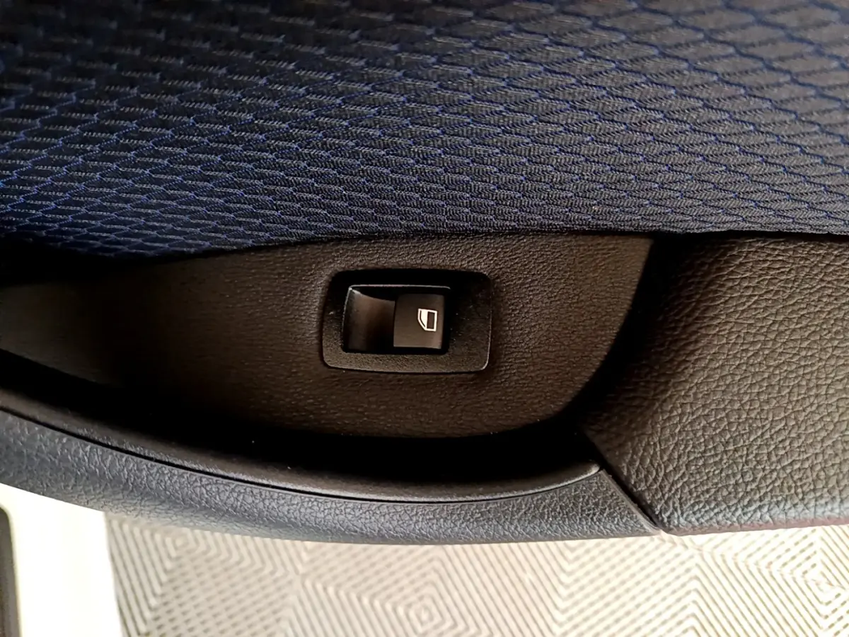 Bouton de commande de lève-vitre intégré dans la garniture intérieure noire d'une BMW X1 blanche, vue en gros plan.