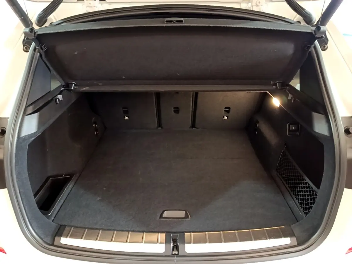 Coffre ouvert vu de l'arrière d'un BMW X1 blanc 2022, avec intérieur noir et éclairage latéral allumé.