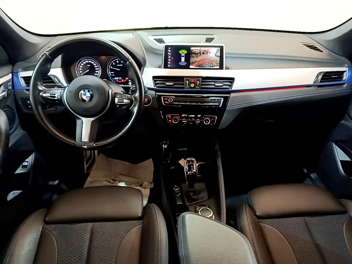 Vue intérieure avant du tableau de bord noir et volant cuir d’une BMW X1 sDrive18i M Sport 2022 avec écran tactile central.