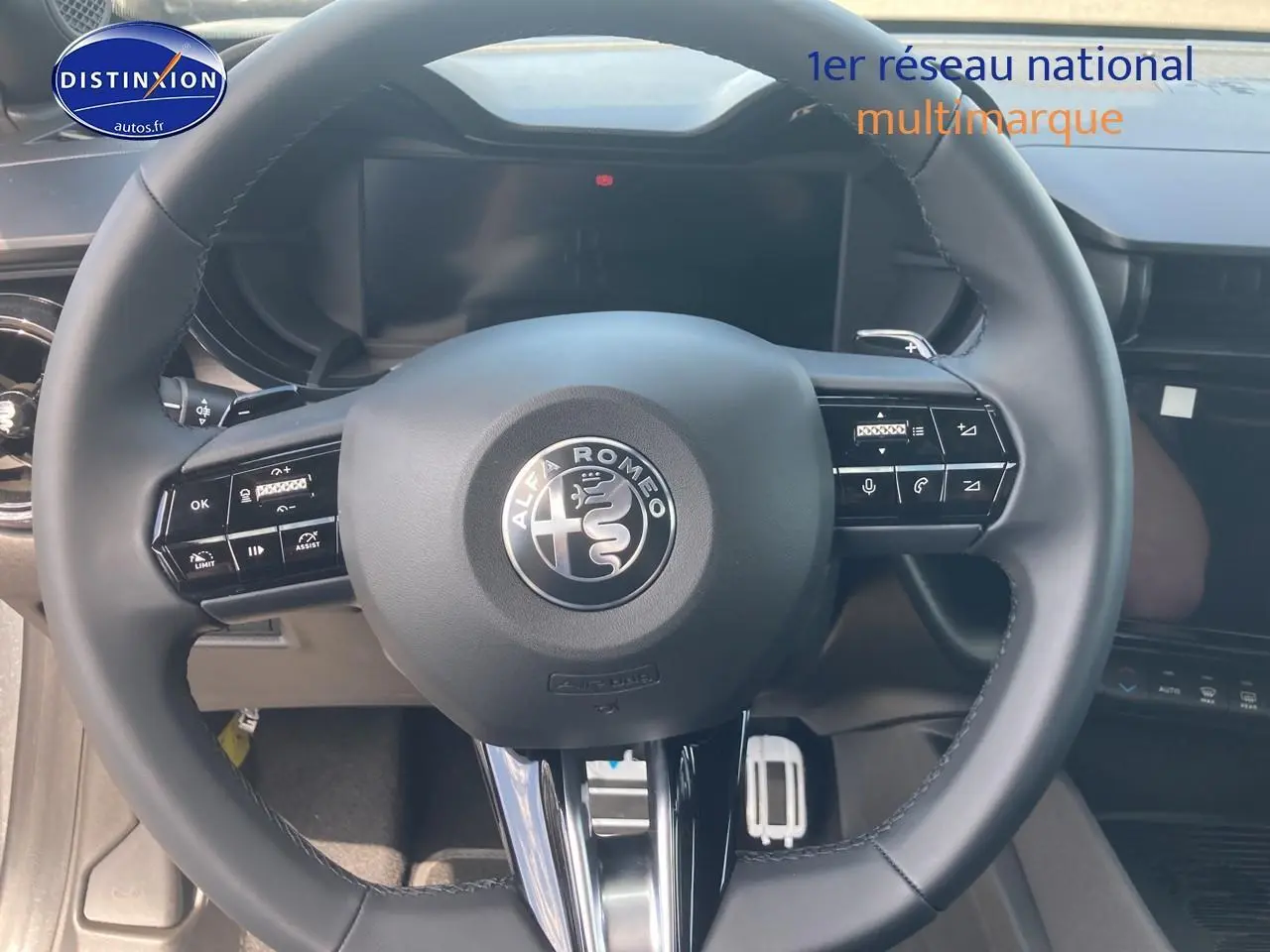 Vue rapprochée du volant noir de l'Alfa Romeo Junior 1.2 hybride 2026 avec commandes intégrées et logo central.