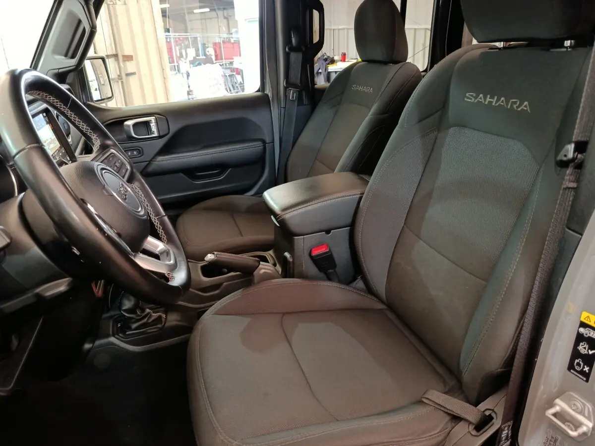Vue intérieure côté conducteur de la Jeep Wrangler Sahara 2022 avec sièges noirs brodés "Sahara" et volant cuir.