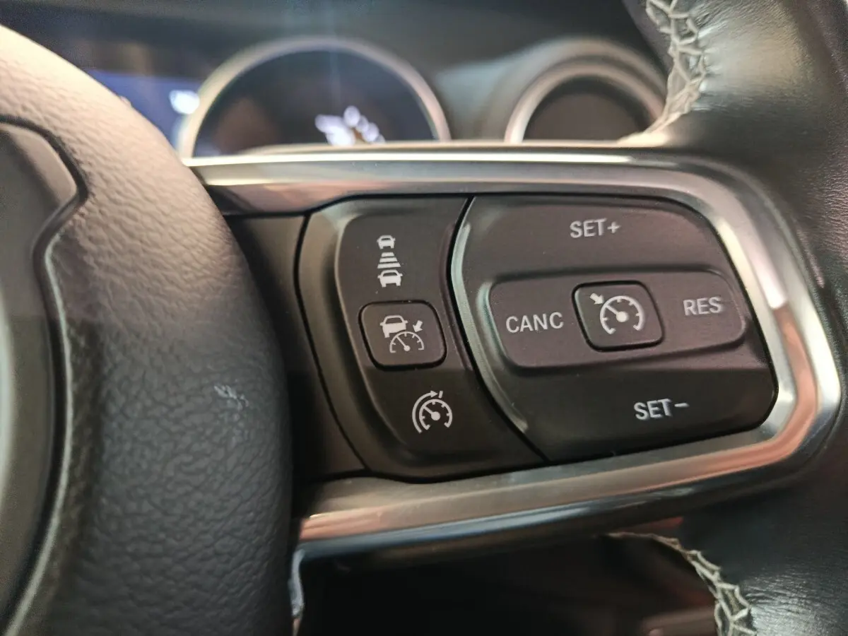 Gros plan sur les commandes du régulateur de vitesse au volant cuir noir de la Jeep Wrangler gris foncé 2022.