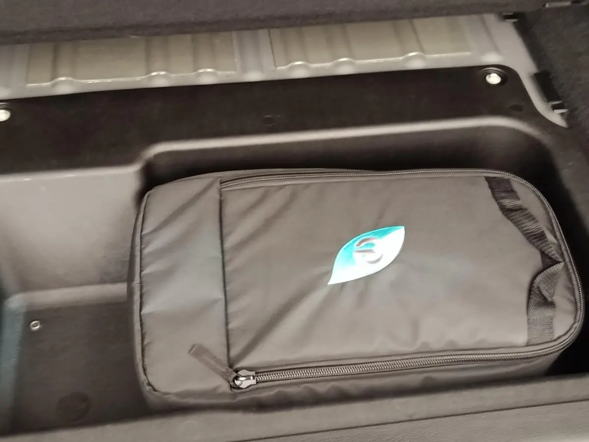 Rangement sous plancher avec sac de charge noir marqué d’un logo bleu dans le coffre d’un Jeep Wrangler gris foncé.