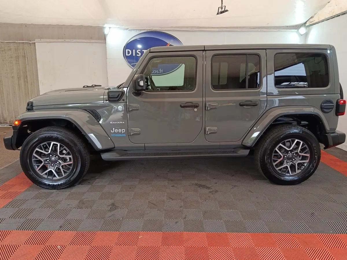 Vue de profil côté gauche d'un Jeep Wrangler Sahara gris foncé hybride rechargeable, avec jantes alliage et toit rigide.