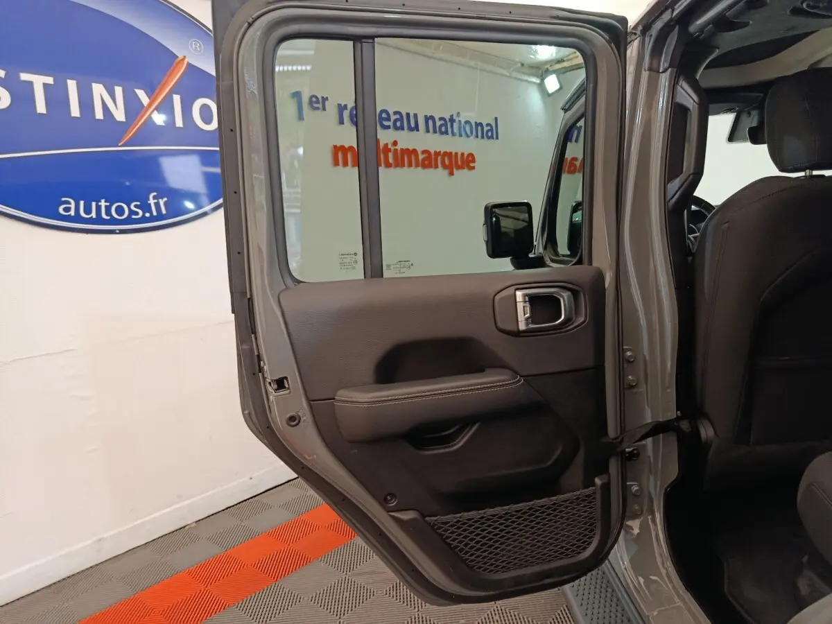 Vue intérieure côté gauche de la porte arrière ouverte d’un Jeep Wrangler gris foncé, avec garniture noire et filet de rangement.