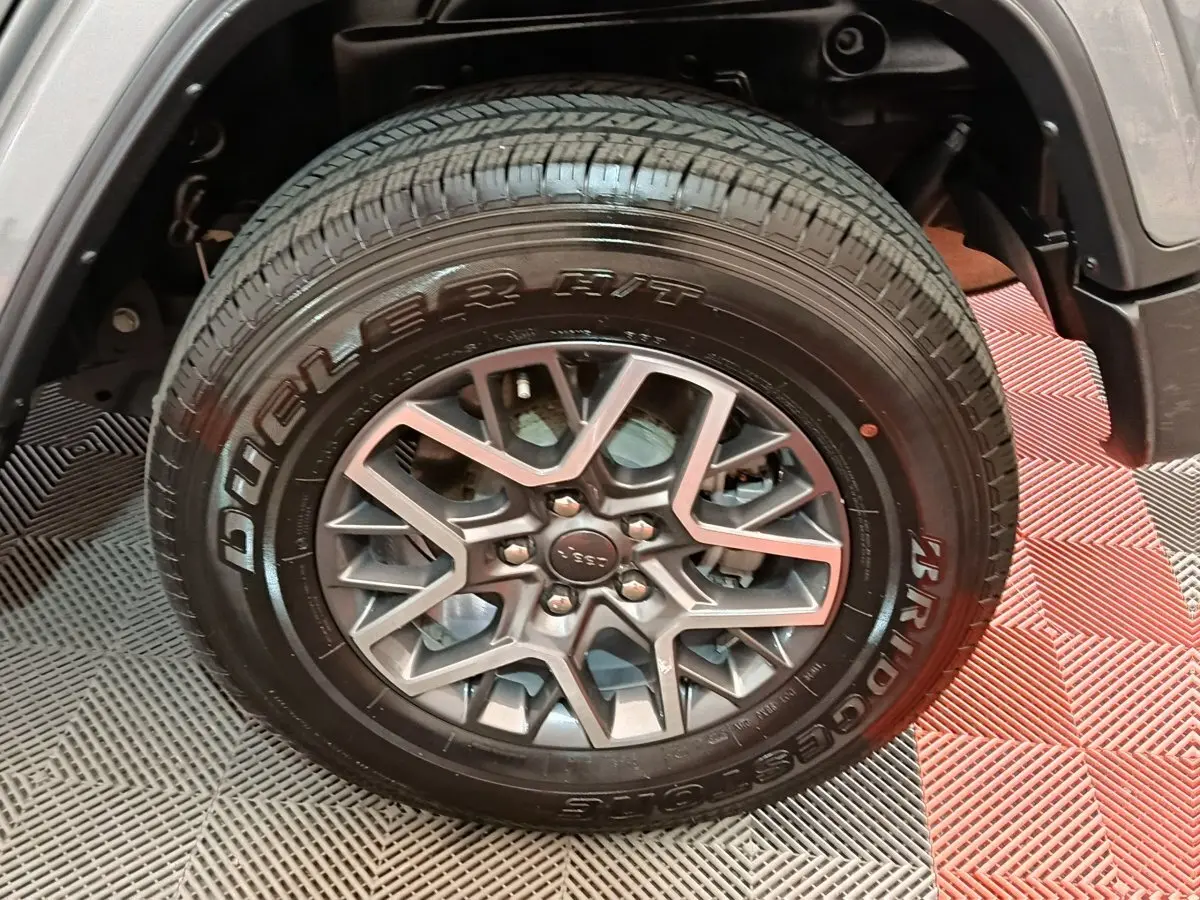 Gros plan sur la roue avant droite du Jeep Wrangler gris foncé, mettant en valeur la jante aluminium et le pneu Bridgestone.