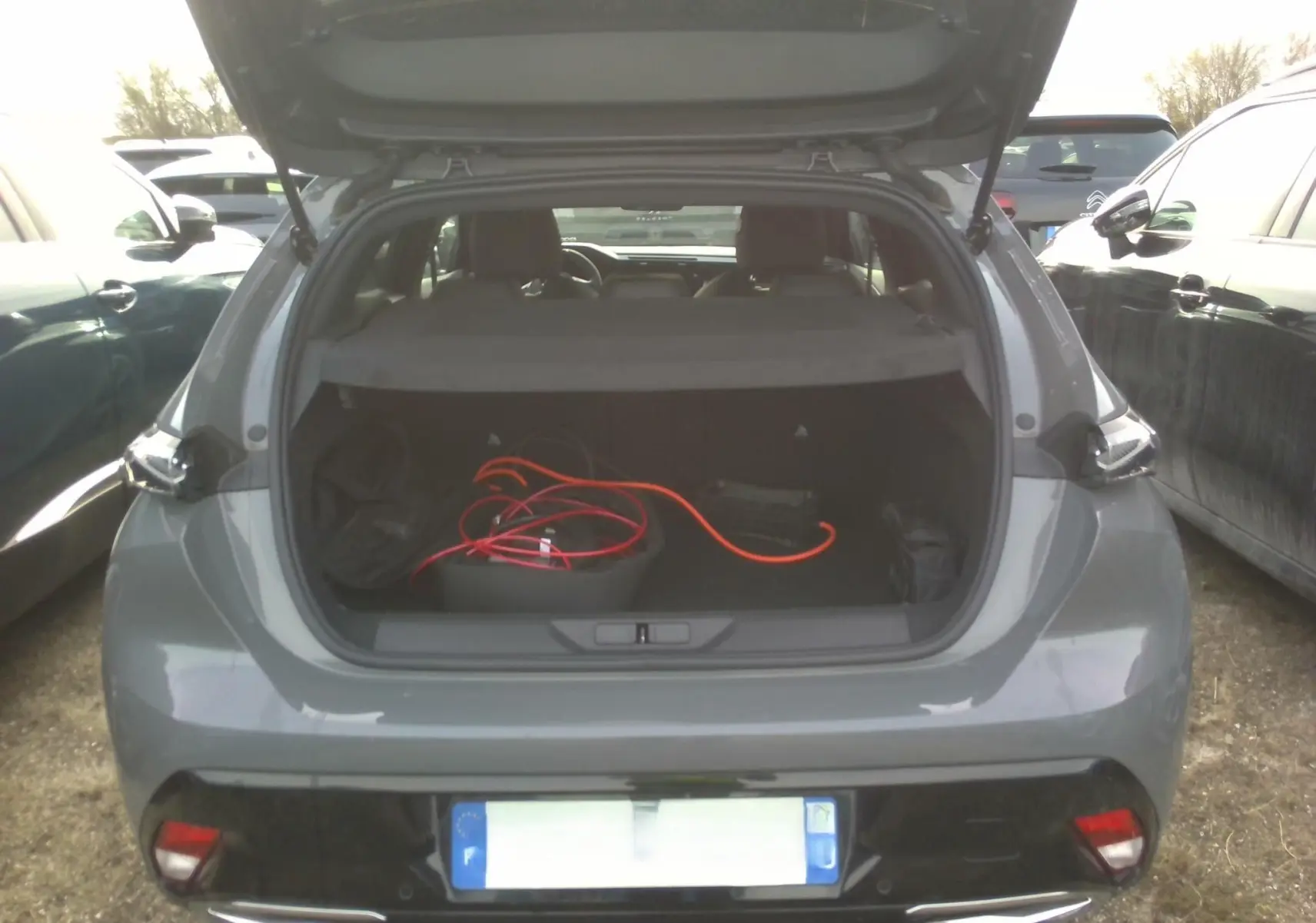 Vue arrière ouverte d'un Peugeot 308 gris clair 2024 avec coffre dévoilant un câble de recharge orange.