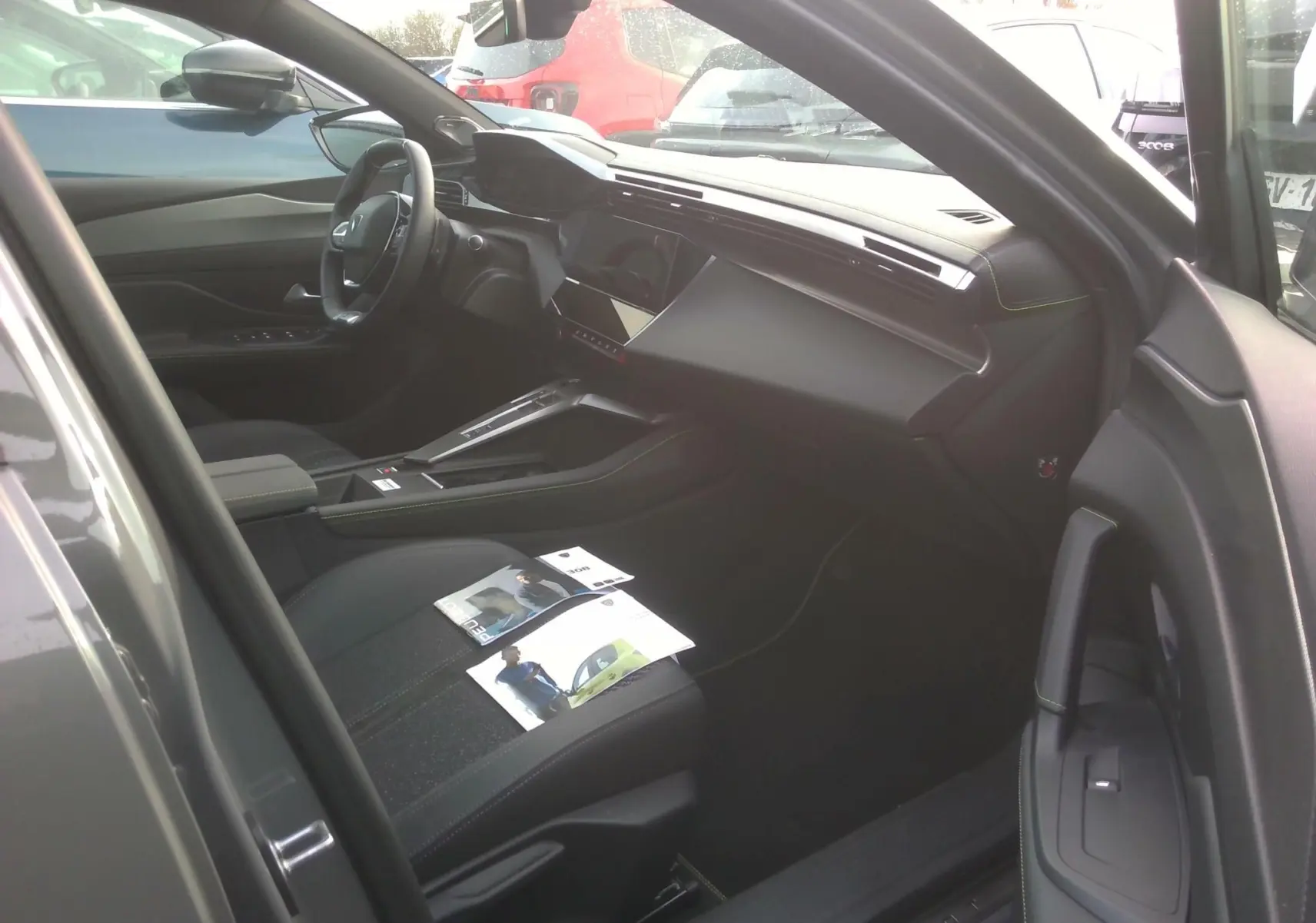 Intérieur noir vu côté conducteur d'une Peugeot 308 gris clair 2024, mettant en valeur le tableau de bord moderne et la console centrale.