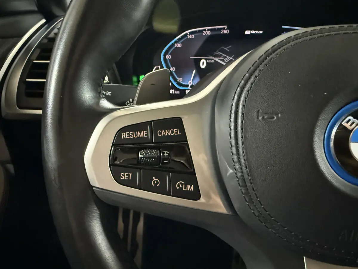 Gros plan sur le côté gauche du volant cuir de la BMW X3 xDrive30e 2023 avec commandes de régulateur de vitesse.