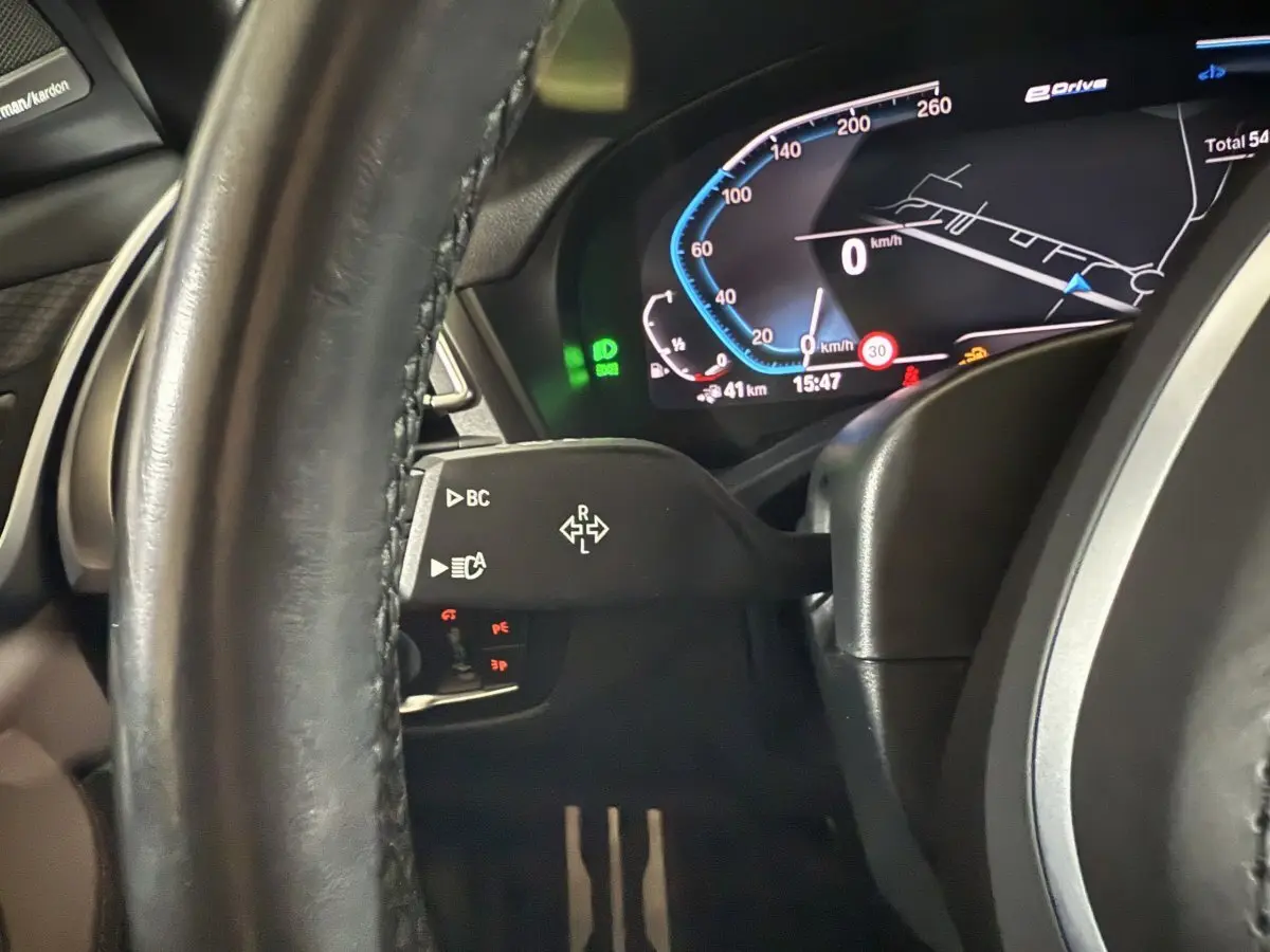 Gros plan sur le tableau de bord numérique et le volant cuir noir de la BMW X3 xDrive30e 2023, affichage vitesse et navigation.