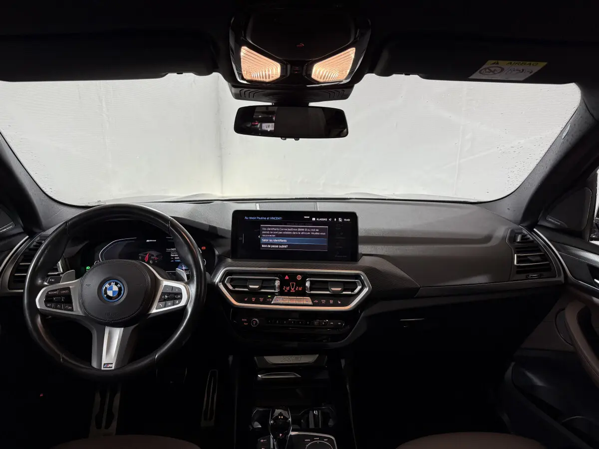 Vue intérieure avant du BMW X3 xDrive30e 2023, tableau de bord noir avec écran tactile central et volant cuir M Sport.